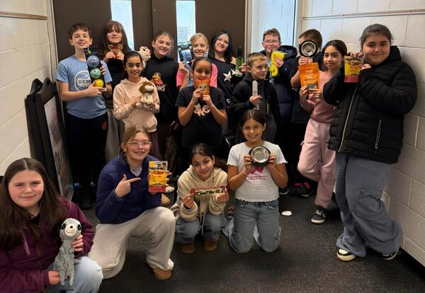 A group of children pose while holding dog collection items like toys, balls, and snacks.