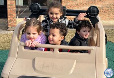 Four children sitting inside a beige plastic play car on a playground