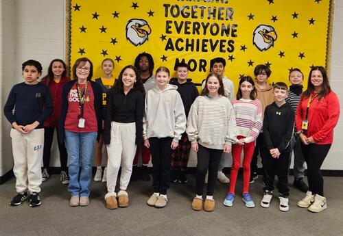 Prairie View Students and Staff of the month pose proudly in front of school bulletin board in hallway