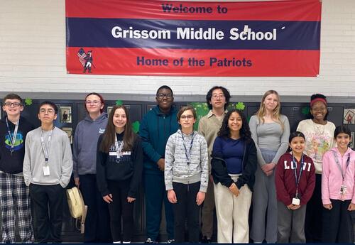 A group of students stands in front of lockers with a banner that reads "Welcome to Grissom Middle School Home of the Patriots".