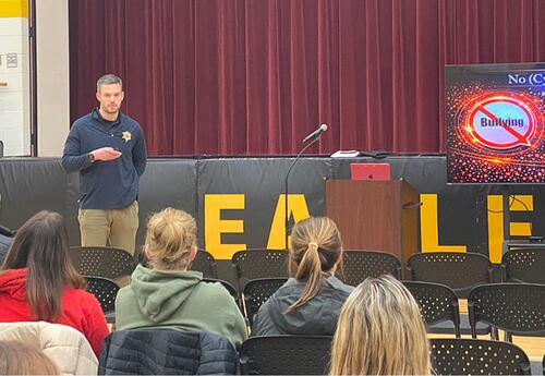 Tinley Park police officer presenting to parents sitting in school gym about cyberbullying