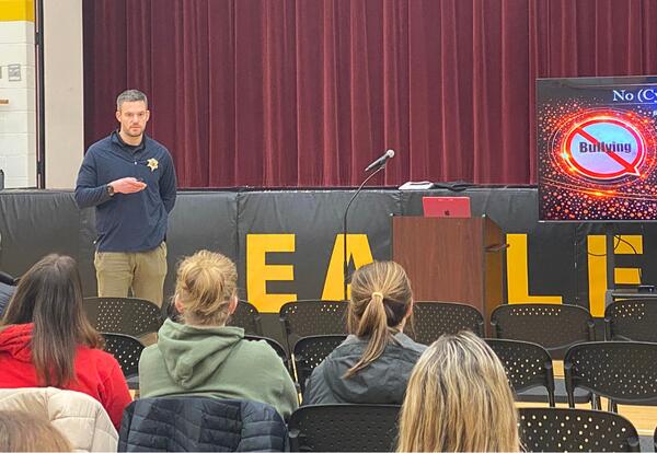 Tinley Park police officer presenting to parents sitting in school gym about cyberbullying