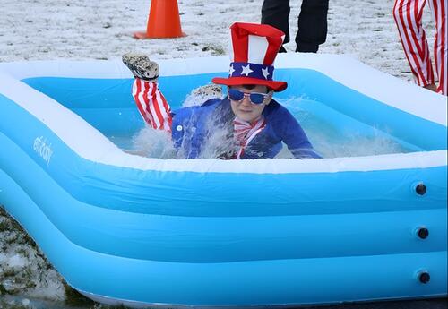 A student wearing a patriotic outfit jumps into an inflatable pool, splashing for Cool School Plunge.
