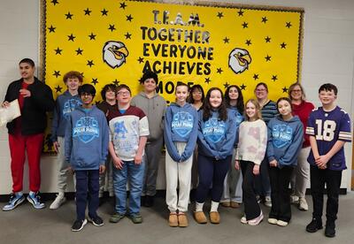 Prairie View Students and Staff of the month pose proudly in front of school bulletin board in hallway