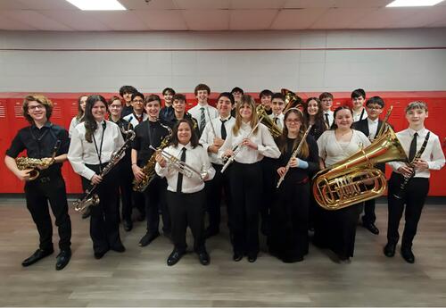 Twenty-three students in formal attire, holding various musical instruments, posing for a photograph in a school hallway at the SWIC Honor Band
