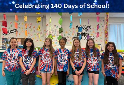 Celebrating 140 Days of School with students wearing matching red, white, and blue tie-dye t-shirts stand in media center decorated with hanging books and butterflies