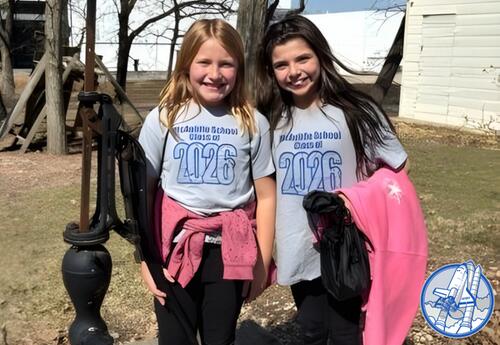 Two children stand in front of an old-fashioned water pump on a class trip.