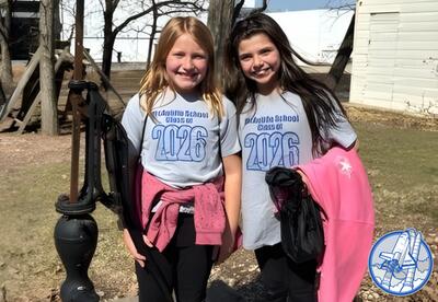 Two children stand in front of an old-fashioned water pump on a class trip.