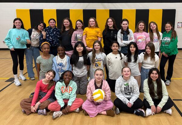 Fifth-grade volleyball team poses in rows for a photo in the school gym.