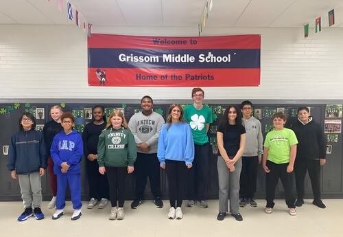A group of students stands in front of lockers with a banner that reads "Welcome to Grissom Middle School Home of the Patriots".