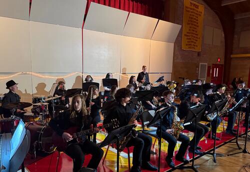 A jazz band performs in a gymnasium, with members playing saxophones, guitars, drums, and keyboard.