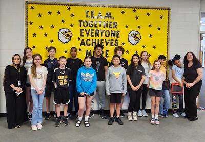 Prairie View Students and Staff of the month pose proudly in front of school bulletin board in hallway