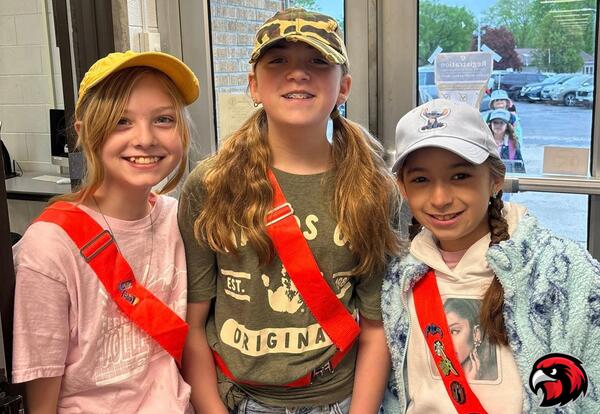 Three young girls wearing red safety harnesses and hats pose for a picture.