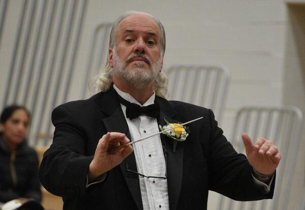 Conductor in a tuxedo leading an orchestra with a baton in hand during a performance.