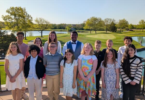 A group of students posing for a picture on a balcony overlooking a golf course.