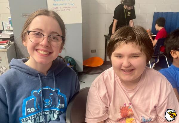 Two children pose and smile together in the classroom.