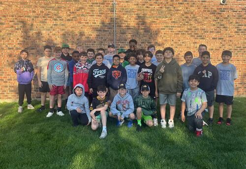 A large group of children pose for a photo in front of a brick building with a grassy lawn in the foreground.