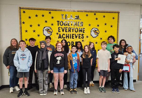 Prairie View Students and Staff of the month pose proudly in front of school bulletin board in hallway