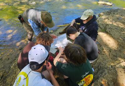A group of people gathered around a piece of paper, near a body of water.