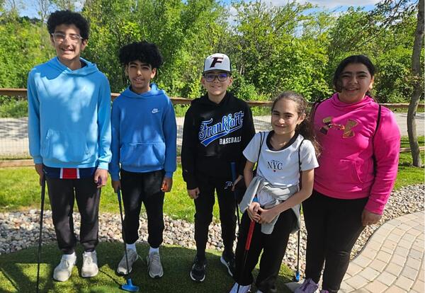 Students pose on miniature golf course holding club on field trip