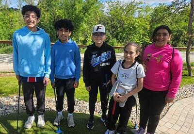 Students pose on miniature golf course holding club on field trip