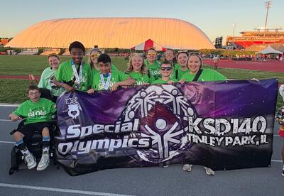Student and staff holding KSD 140 Special Olympics banner at summer games