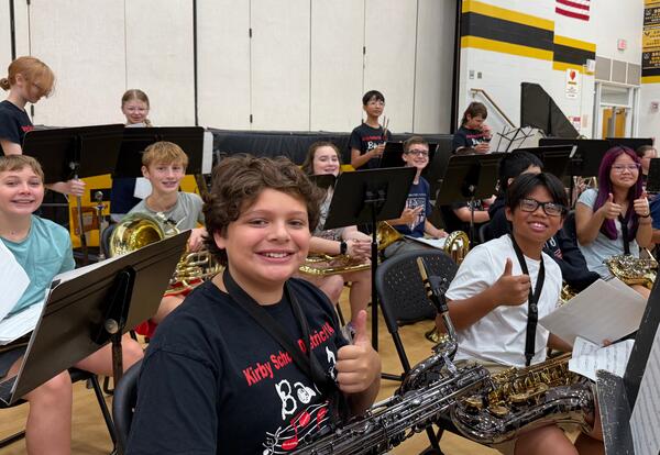 Band camp students sitting in gym with instruments smiling at camera