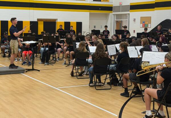 Band members playing instruments while conductor leads them during showcase for fifth graders