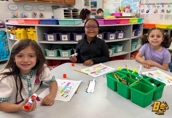 Three students smile with sitting at table working on a project in the classroom
