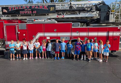 Students line up in front of fire truck parked outside of school