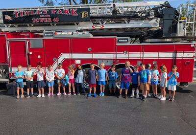 Students line up in front of fire truck parked outside of school