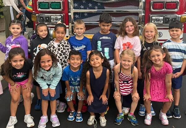 Group of students standing in two rows in front of fire truck outside of school