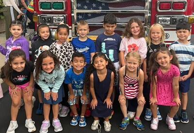 Group of students standing in two rows in front of fire truck outside of school