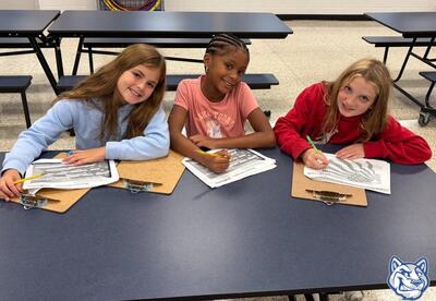 Three students smile while sitting at table working on project
