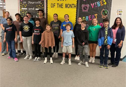 Students and staff of the month pose in front of school bulletin boards in hallway