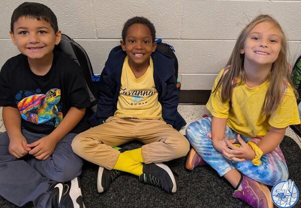 Three students sitting in hallway smiling for World Smile Day