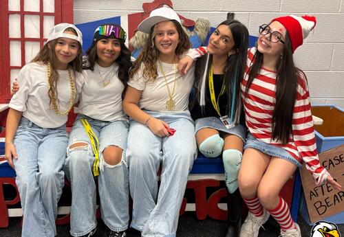 Middle school students sitting on bench dressed in costumes during Halloween dance