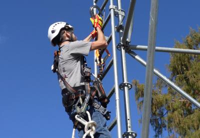 A student wearing a safety harness with clip hooks practices climbing safety on a ladder.
