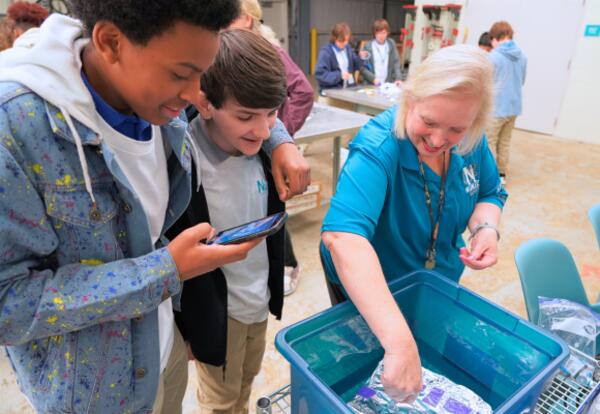 Visiting high school students watch Nunez STEAM Director Julie Rexford perform a science experiment.