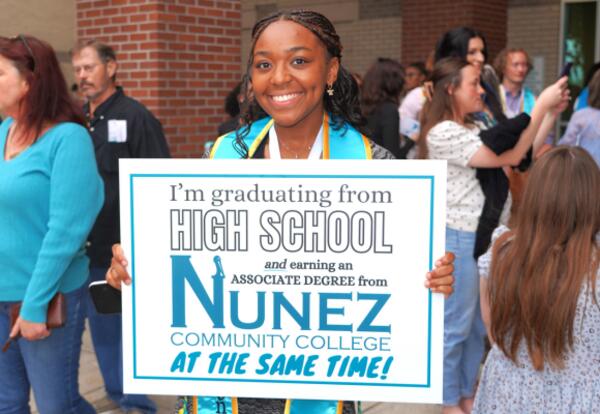 A Dual Enrollment graduate is shown holding a yard sign for associate degree recipients outside the Awards Ceremony