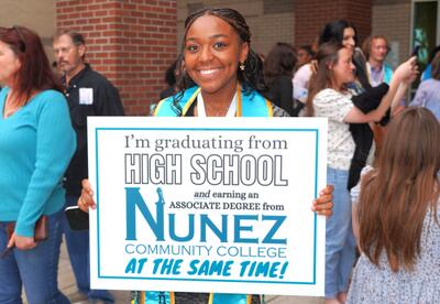 A Dual Enrollment graduate is shown holding a yard sign for associate degree recipients outside the Awards Ceremony