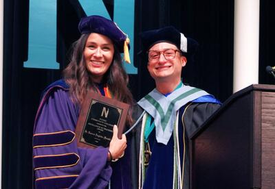 Dr. Lauren Englade-Franklin accepts the 2026 Excellence In Teaching Award from the 2025 winner, Dr. Charles Miller, onstage at Nunez's 2026 Commencement Ceremony.