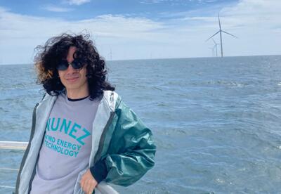 Nunez Wind program student Walker Argao is pictured on a boat trip to visit an offshore wind farm. Wind turbines are visible in the distance.
