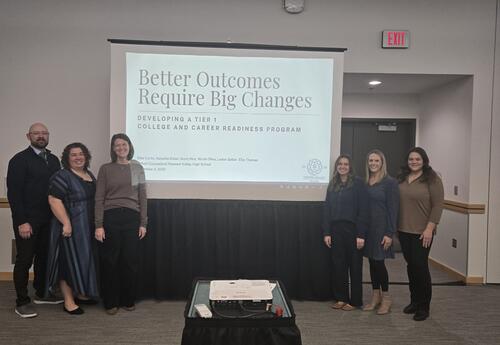 Pleasant Valley High School counselors stand together in front of a presentation screen at the Iowa School Counselor Association Conference. The screen displays the title “Better Outcomes Require Big Changes: Developing a Tier 1 College and Career Readine
