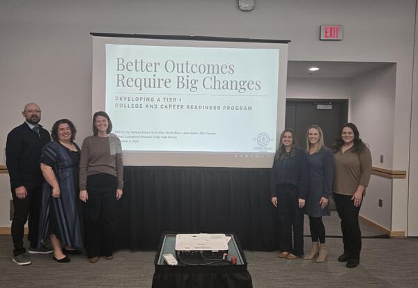 Pleasant Valley High School counselors stand together in front of a presentation screen at the Iowa School Counselor Association Conference. The screen displays the title “Better Outcomes Require Big Changes: Developing a Tier 1 College and Career Readine