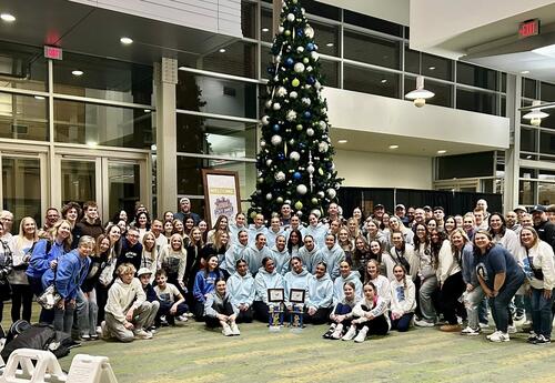 Pleasant Valley Platinum dancers pose with their coaches, families, and supporters in front of a decorated tree at the 2025 State Dance Competition, celebrating together after the event.