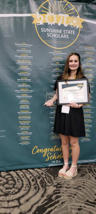 Madalyn Sapia in front of Sunshine State Scholars banner