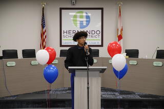 Santiago Pinkney speaking behind a podium in the board room
