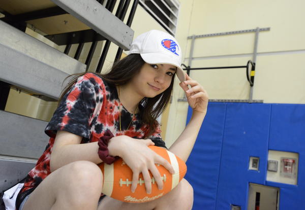 Picture of a Myers student sitting on the bleachers in the gym with a football.