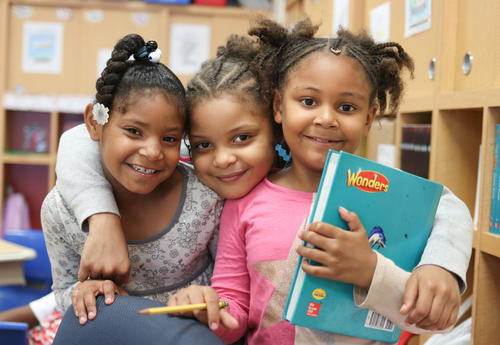 Three students posing for a picture while holding a Wonder ELA textbook.